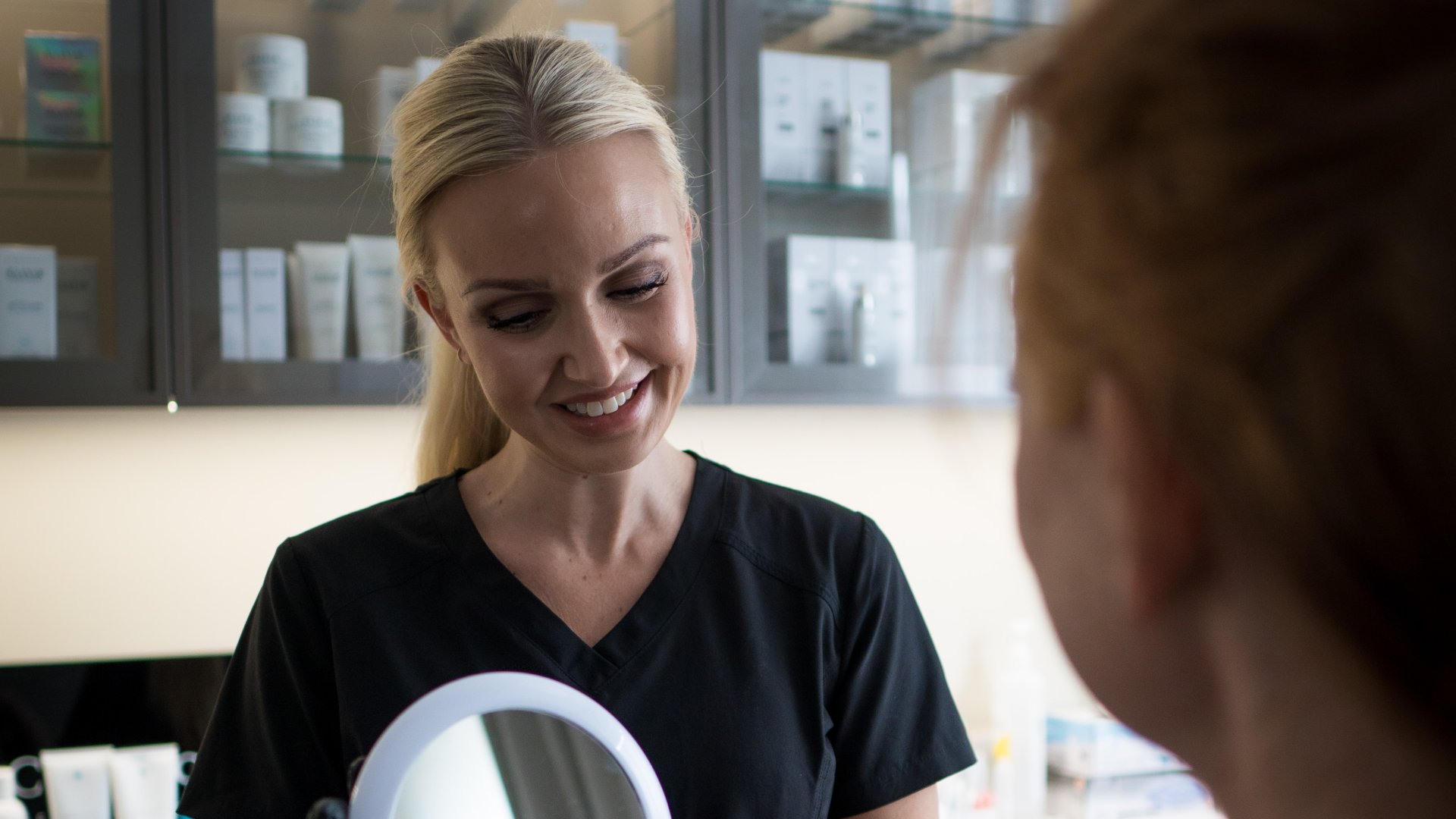 Kosmetisk dermatologisk sykepleier Celine Seeberg smiler med pasient foran speil
