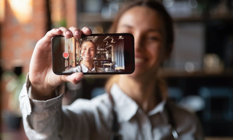 Smilende jente holder mobilen foran seg med seg selv på skjermen