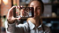 Smilende jente holder mobilen foran seg med seg selv på skjermen
