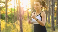Ung kvinne jogger i skogen med mobil og ørepropper