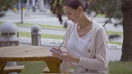 Sonja sitter på en benk og ser på mobil