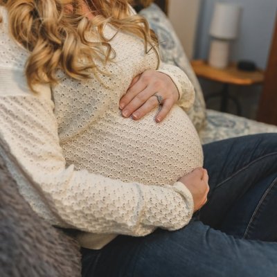Gravid kvinne i sofa holder rundt magen
